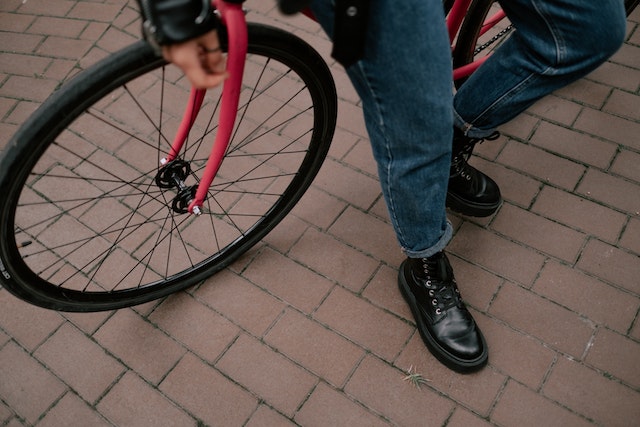 Person in Blue Denim Jeans and Black Leather Shoes Standing Beside Black and Red Bicycle